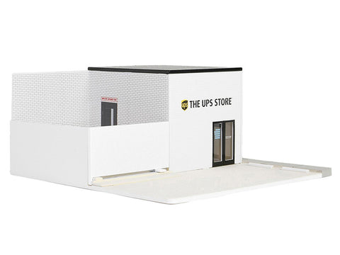 Diorama of a White building with the UPS logo and the words "THE UPS STORE" above the door, with 2 parking space in front of the building and a fenced in section next to the building.