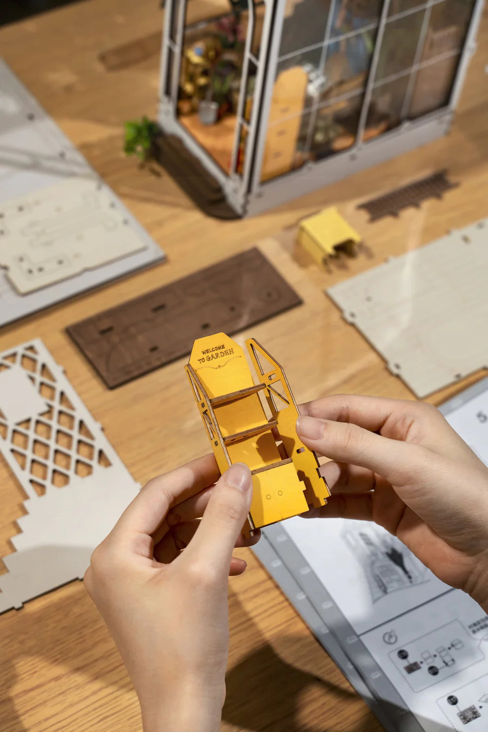 Person assembling a yellow model piece with laser cut pieces on table behind.