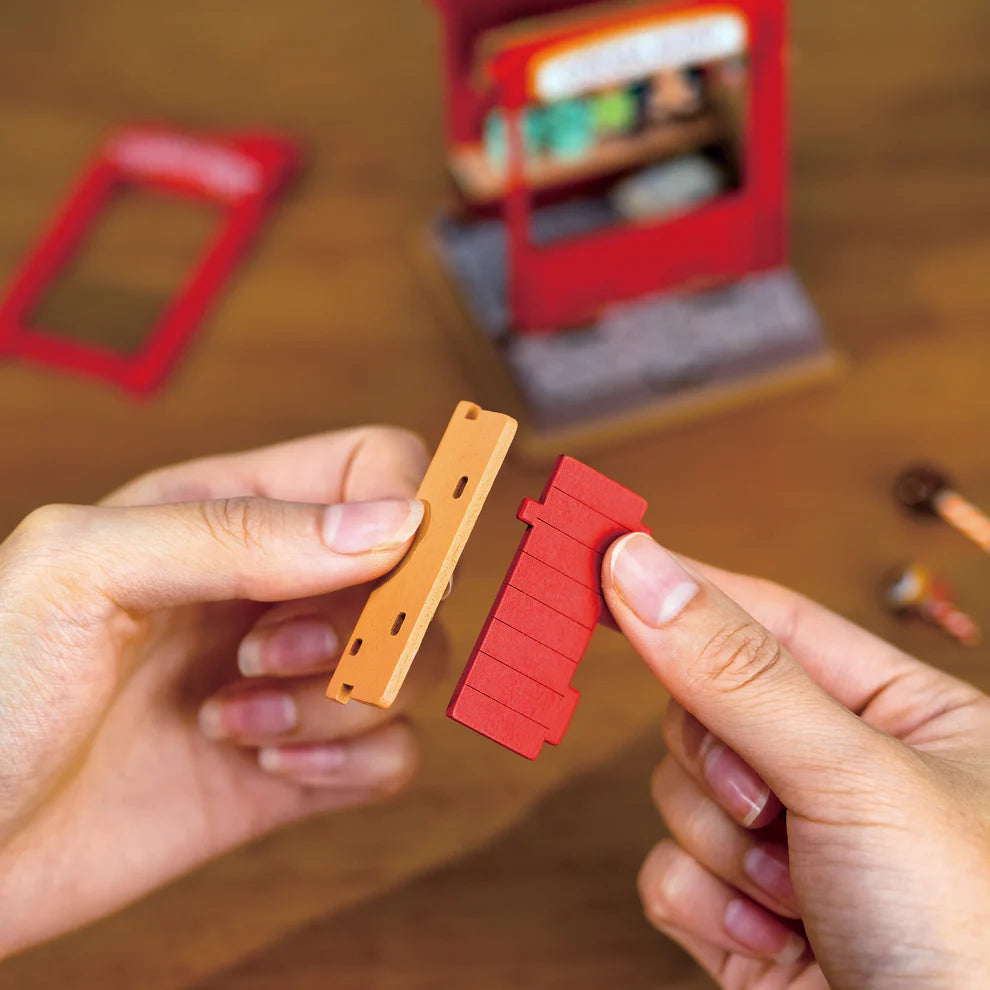 Two hands holding a red and an orange plastic component on a blurred background with tools.