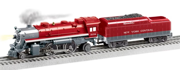 A red and gray toy train model representing the New York Central Lionchief 2-4-2 locomotive, with visible smoke coming from the engine.