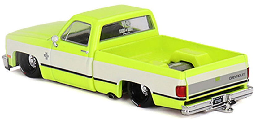 1/64 scale diecast model of a yellow Chevrolet Silverado with white stripe on sides and lowrider chassis.
