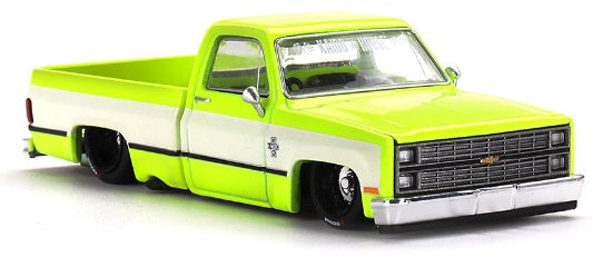 1/64 scale diecast model of a yellow Chevrolet Silverado with white stripe on sides and lowrider chassis.