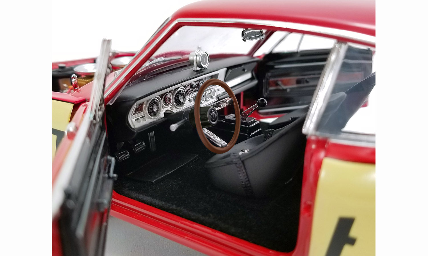 Close-up of a model car's interior with a red exterior, featuring a steering wheel and dashboard.