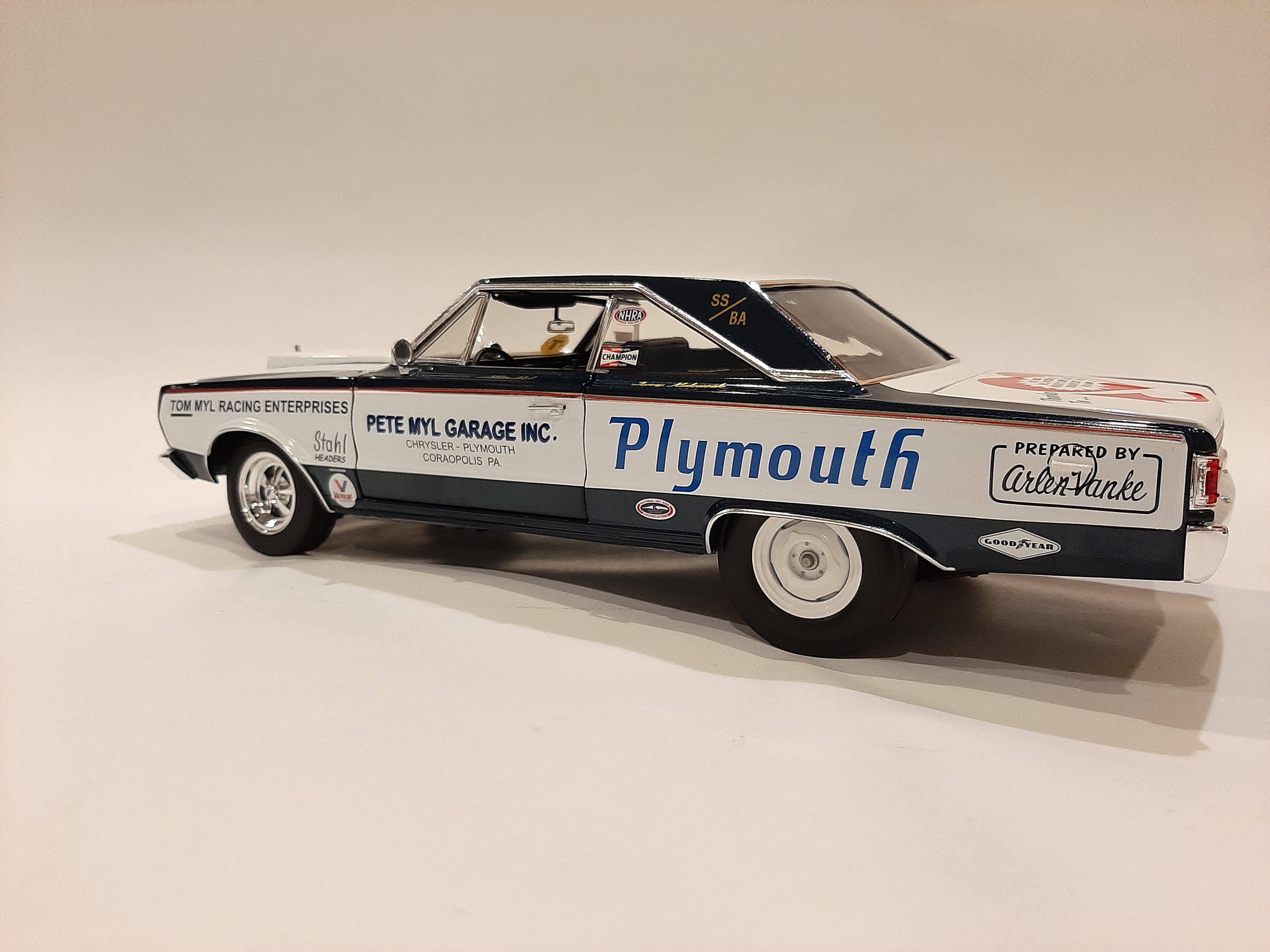 A 1/18 scale model of a 1967 Plymouth Belvedere in white with blue and black detailing, resembling a racing car with sponsor decals.