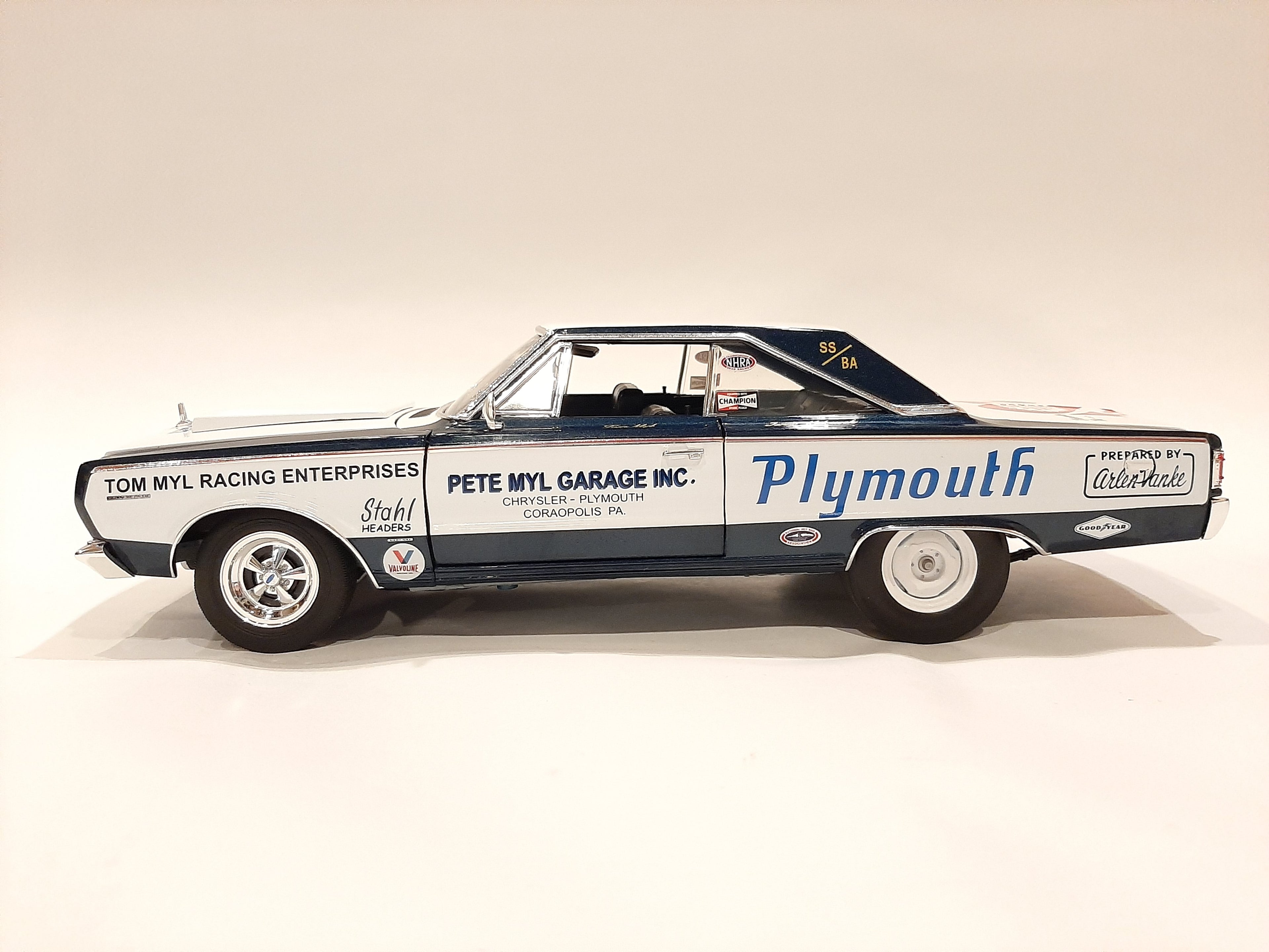 A 1/18 scale model of a 1967 Plymouth Belvedere in white with blue and black detailing, resembling a racing car with sponsor decals.