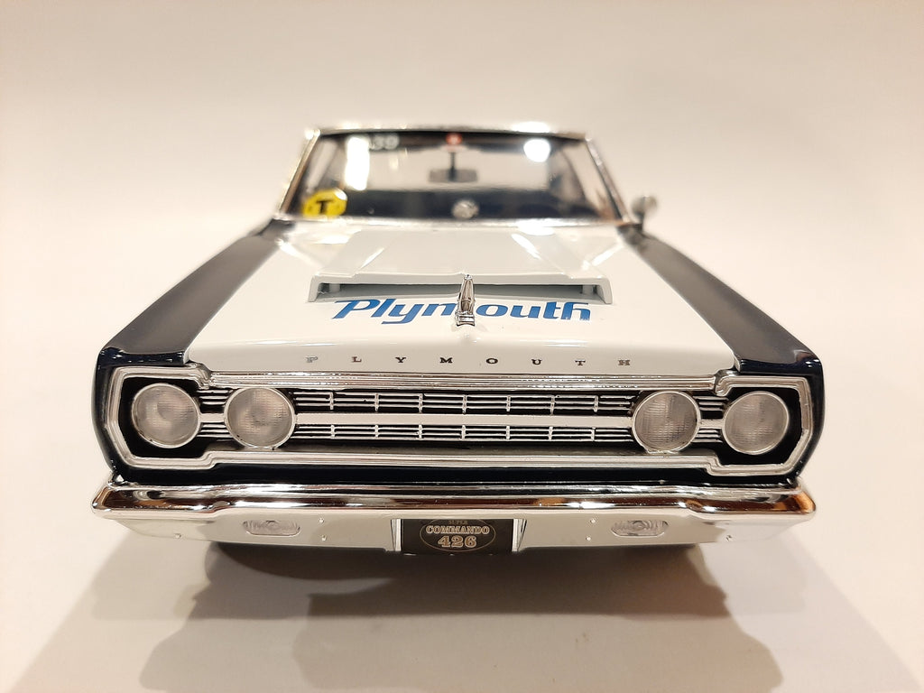 A 1/18 scale model of a 1967 Plymouth Belvedere in white with blue and black detailing, resembling a racing car with sponsor decals.
