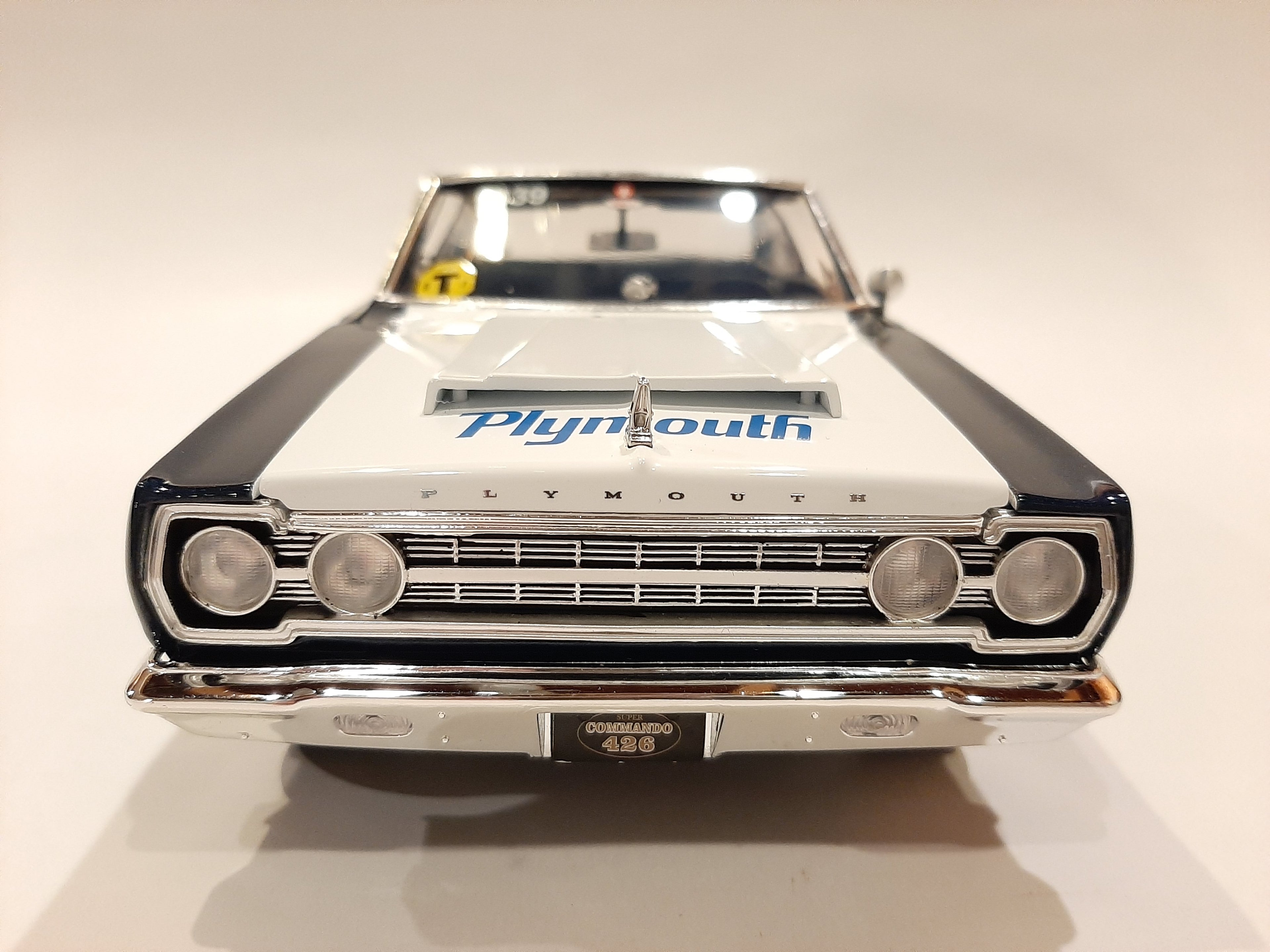 A 1/18 scale model of a 1967 Plymouth Belvedere in white with blue and black detailing, resembling a racing car with sponsor decals.