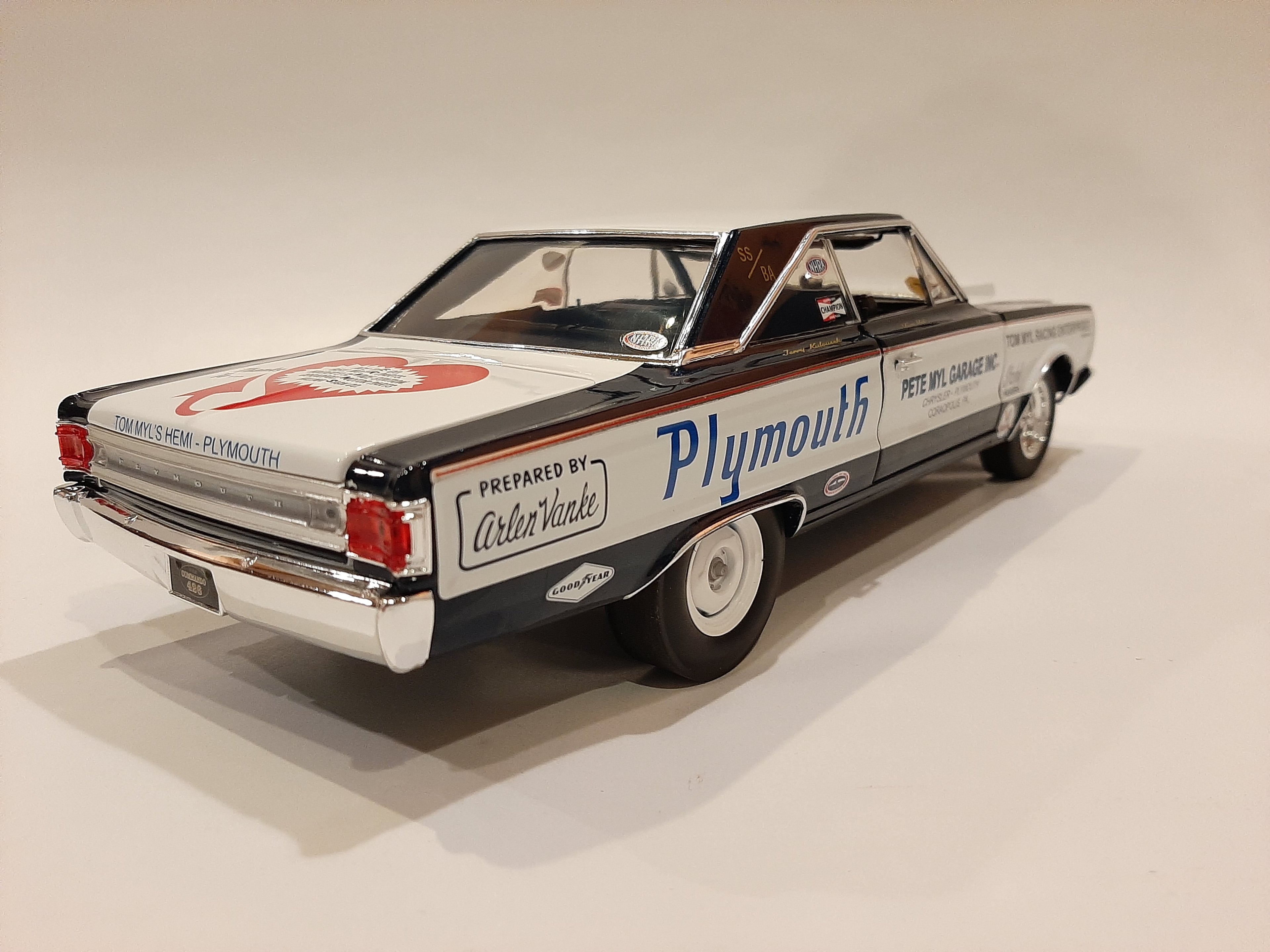 A 1/18 scale model of a 1967 Plymouth Belvedere in white with blue and black detailing, resembling a racing car with sponsor decals.