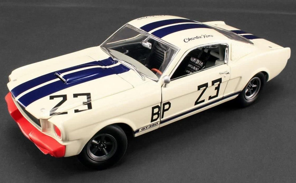 A 1/18 scale model of a 1965 Ford Shelby Mustang GT350 R with a white and blue striped paint scheme, featuring the number 23 and the name 'Charlie Kemp'.