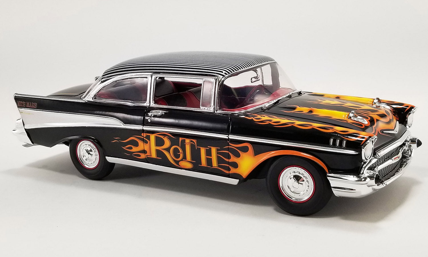1/18 scale diecast model of 1957 Chevrolet Bel Air in black with flames painted on the sides and hood and "ROTH" on the doors.