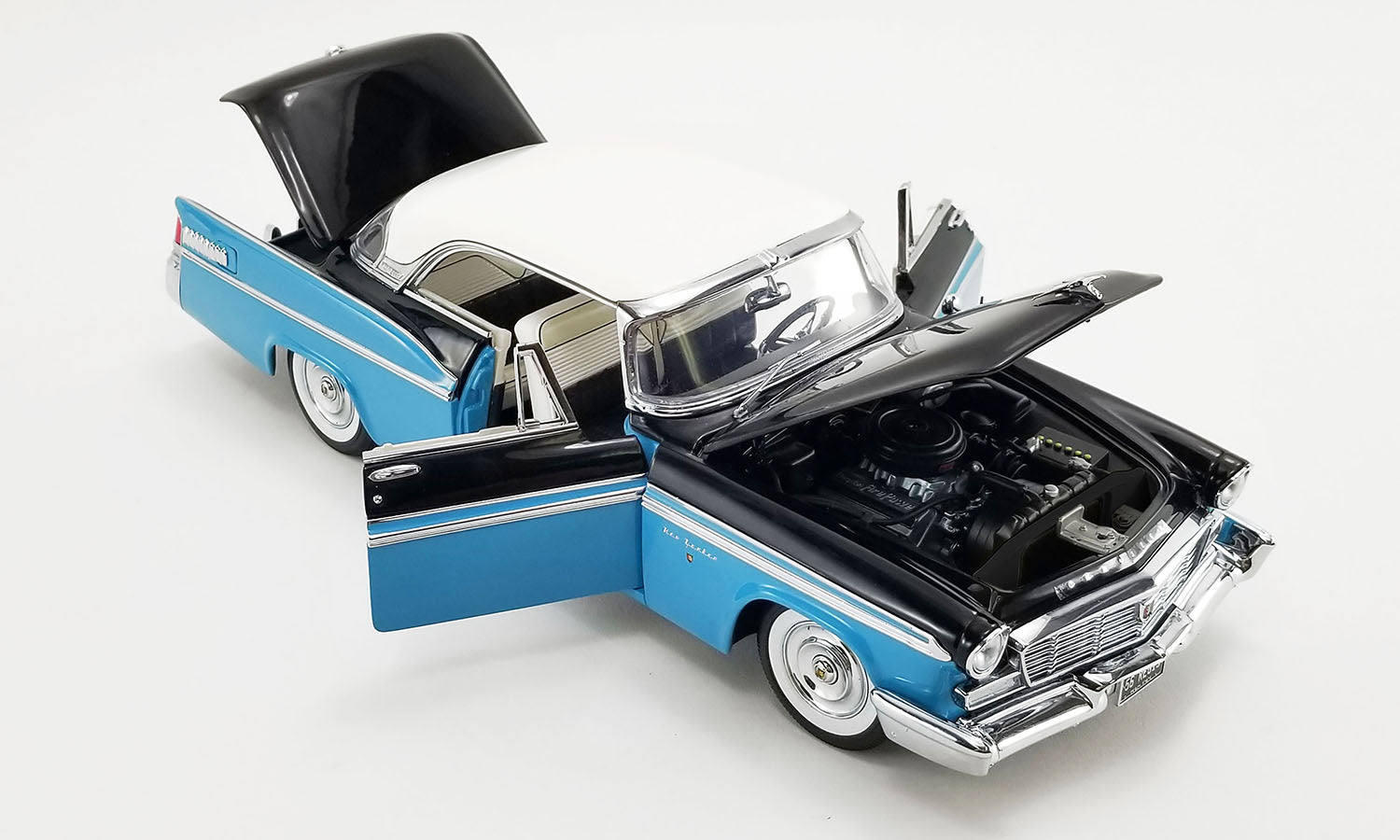 A 1/18 scale model of a 1956 Chrysler New Yorker St. Regis in Stardust Blue and black with a white roof showing open doors, hood, and trunk.