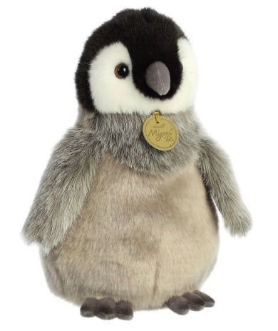 A plush emperor penguin chick with a grey and black body, wearing a yellow tag around its neck.