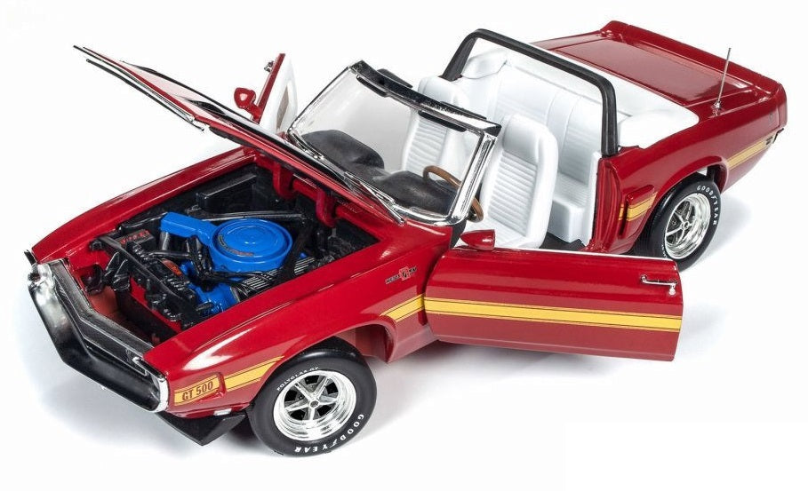 A 1/18 scale model of a 1970 Ford Shelby GT500 Convertible in red color with yellow stripe and white interior.  Convertible roof, hood, and doors are open.