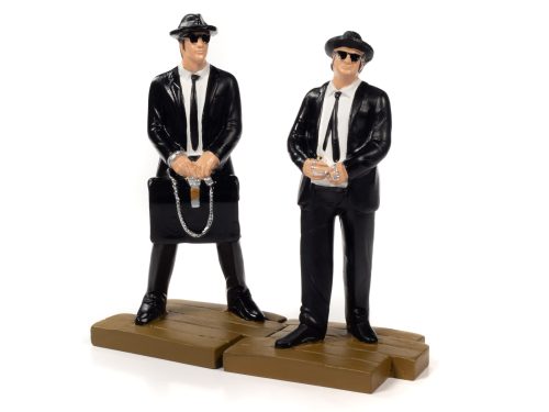 Two figures dressed in all black suits with sunglasses, hats, and one has a brief case.  The figures have bases that looks like fake wood.